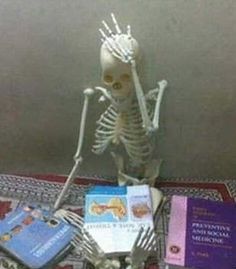 a skeleton sitting on top of a table next to some books and a book bag