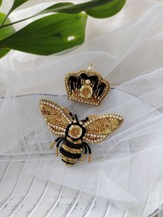 two gold and black bee brooches sitting on top of a white cloth covered table