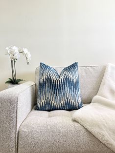 a blue and white pillow sitting on top of a couch next to a vase with flowers