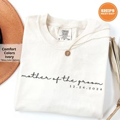 a white shirt with the words mother of the groom printed on it next to a hat