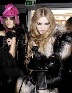 two women dressed in black and white furs, one with a pink helmet on her head