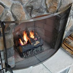 a fire is burning in a fireplace with rocks on the sides and logs around it