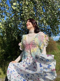 a woman is sitting under a tree wearing a white dress with colorful flowers on it