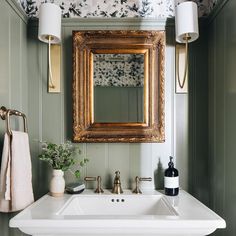 a bathroom sink sitting under a mirror next to a wall mounted faucet and a bottle of wine