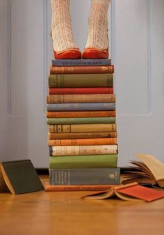 a stack of books sitting on top of a wooden table next to a pair of red shoes