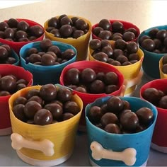 there are many small bowls with chocolate candies in them on the table and one has a dog bone