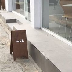 a sign sitting on the side of a building next to a sidewalk with chairs in front of it