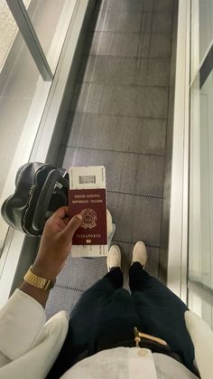 a person sitting on an escalator with their feet up and holding a passport