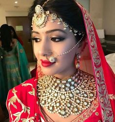 a woman wearing a red and gold bridal outfit with jewelry on her head, in front of other women