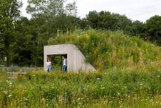 two people standing in front of a building with grass growing on it's side