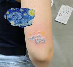 a woman's arm with the starry night tattoo on it, which is painted in blue and yellow