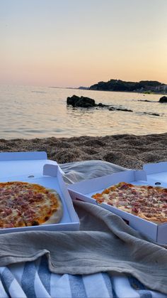 two pizzas sitting on top of a beach next to the ocean