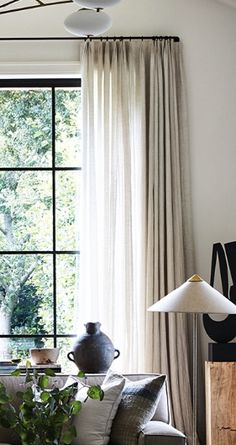 a living room filled with furniture and a large window covered in white curtained drapes