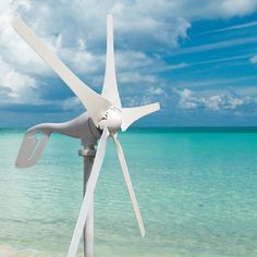 a white wind turbine sitting on top of a sandy beach next to the ocean under a cloudy blue sky