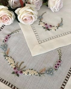 some white and pink roses are on a table with a cross stitched heart in the middle