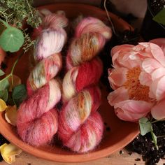 several skeins of dyed wool sit in a bowl next to flowers and peonies