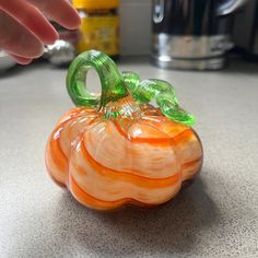 an orange glass pumpkin sitting on top of a counter next to a person's hand