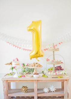 a table topped with cake and desserts under a number one balloon in the air