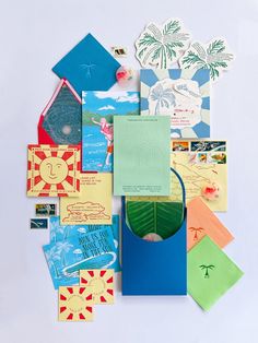 many different types of cards and envelopes on a white surface with palm trees in the background