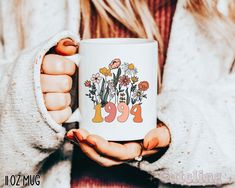 a woman holding a coffee mug with flowers on it in her left hand and the words pee written below