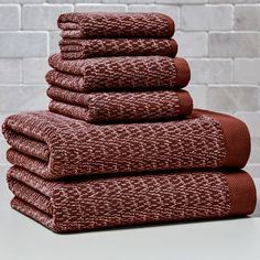 six towels stacked on top of each other in front of a brick wall with white bricks