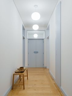 an empty hallway with white walls and wood flooring is seen in this image, there are two wooden benches on either side of the hall