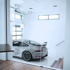 a white sports car is reflected in the glass wall of a modern building with wood flooring