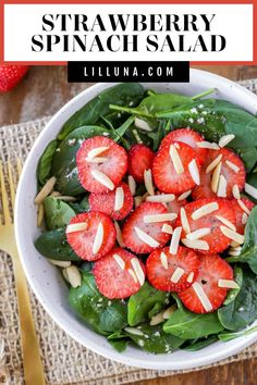 strawberry spinach salad with almonds in a white bowl on top of a table