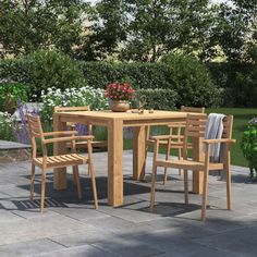 a wooden table and chairs sitting on top of a stone floor next to flowers in a pot