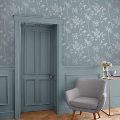 an empty chair in front of a blue wall with white flowers on it and a wooden floor