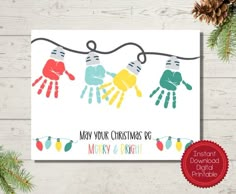 a christmas card with handprints hanging on a string and pine cones in the background