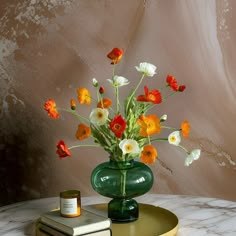 a green vase filled with colorful flowers on top of a table next to two books