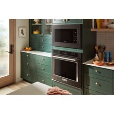 a kitchen with green cabinets and two microwaves on the wall, one built in