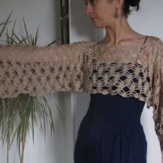 a woman is wearing a crocheted shawl and standing next to a potted plant