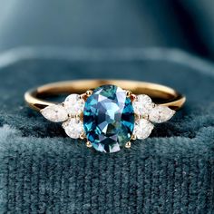 an oval blue and white diamond ring with three pear shaped diamonds on the side, set in yellow gold