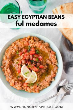 a bowl filled with beans and garnished with lemon wedges next to some pita bread