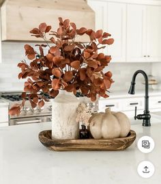 a white vase filled with flowers sitting on top of a counter next to a wooden tray