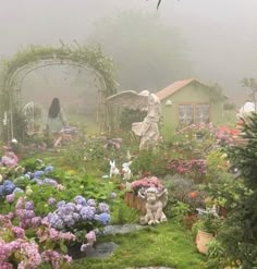 a garden filled with lots of flowers next to a lush green forest covered in fog