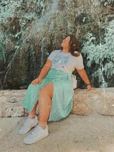 a woman sitting on a stone wall with trees in the background