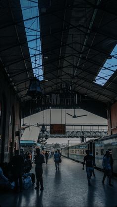 people are walking around in an indoor train station with many lights hanging from the ceiling