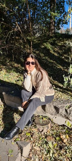 a woman sitting on top of a stone bench in the woods with her legs crossed