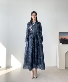 a woman standing in front of a white wall wearing a blue dress with flowers on it