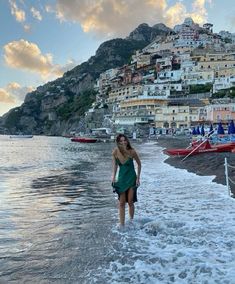 a woman standing in the ocean next to a beach with boats and houses on it