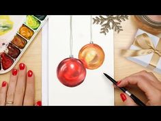 someone is painting christmas ornaments on a paper with watercolors and paintbrushes