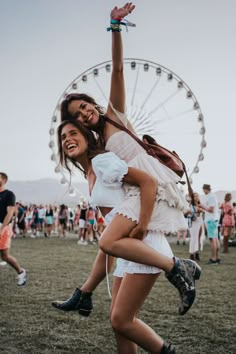 two young women are dancing in front of a ferris wheel at an outdoor music festival