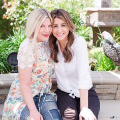 two women sitting next to each other on a bench in front of a bird feeder