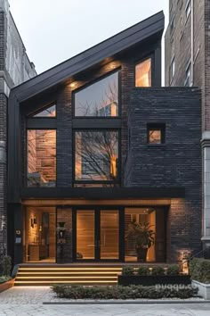 a modern house with large windows and steps leading up to the front door, surrounded by tall brick buildings