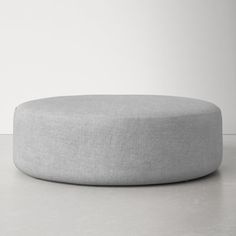 a round grey ottoman sitting on top of a white floor next to a gray wall