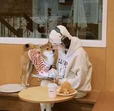 a woman sitting at a table with a dog on her lap and food in front of her