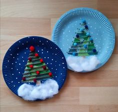 two paper plates decorated with christmas trees and clouds on wooden floored surface, side by side